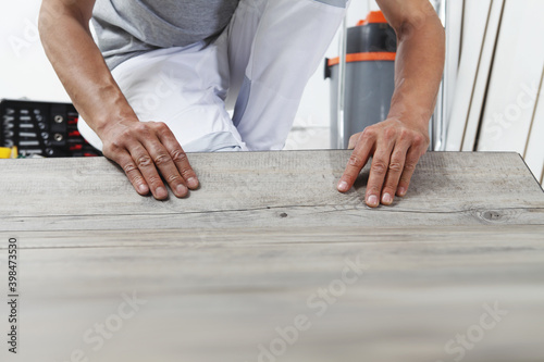 Worker hands installing timber laminate vinyl floor. Wooden floors house renovation.