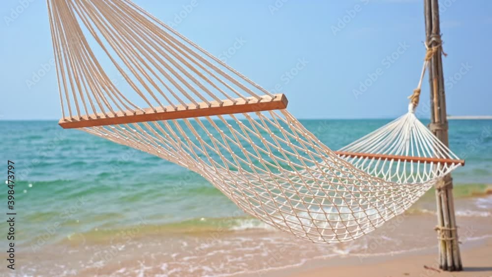 Empty hammock, Rope hammock swinging in the gentle summer breeze blowing along the sandy coast. Breathtaking view of the turquoise ocean waves behind the empty hammock on a tropical island