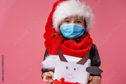 little smiling girl in Santa hat and mask, with Christmas gift box in shape cow. photo