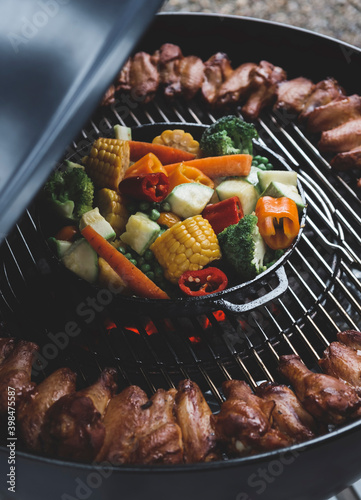 Assorted vegetables and chicken wings on a charcoal grill. Cooking process