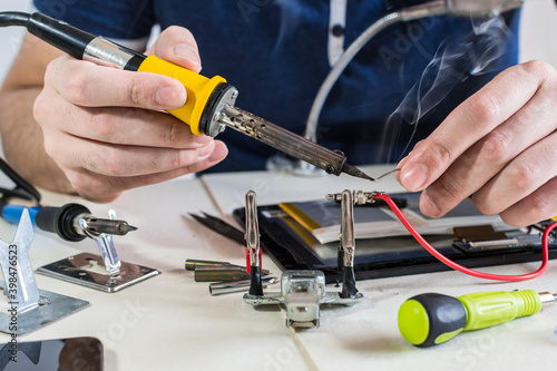 Male hands soldering a cable to electronic device.