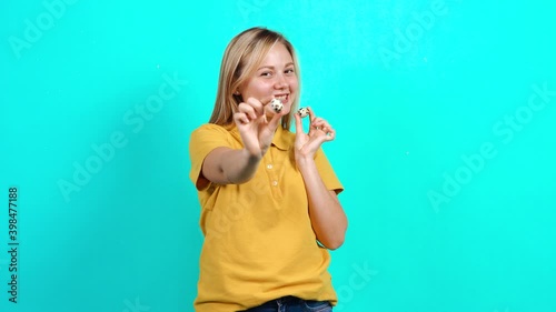 The young woman holding two quail eggs in her hands, promoting the small business. Beautiful Caucasian woman in yellow t-shirt and long blond hair standing on blue background. A fat teenager photo