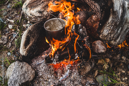 Kettle stands on fire. Cooking food at fire in wild. Beautiful big log burns in bonfire close-up. Survival in wild nature. Wonderful flame with caldron. Pot is on flames. Campfire background.