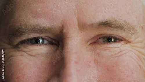 Face of happy elderly middle aged man smiling with friendly blue eyes. Handsome mature male senior citizen with wrinkles on attractive face looking and laughing at camera.  Macro extreme close up, 4K.