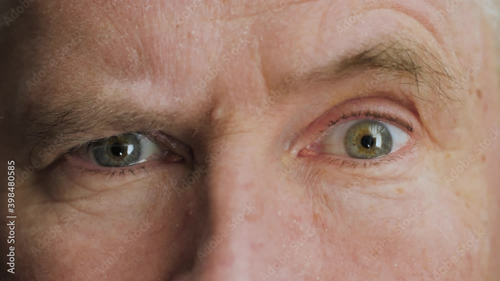 Face of surprised or doubtful elderly middle aged man raising eyebrow. Skeptical mature male senior citizen with wrinkles on attractive face looking at camera. Slow motion, macro extreme close up, 4K.