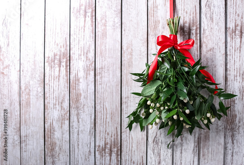 Mistletoe bunch with red bow hanging on white wooden wall, space for text. Traditional Christmas decor