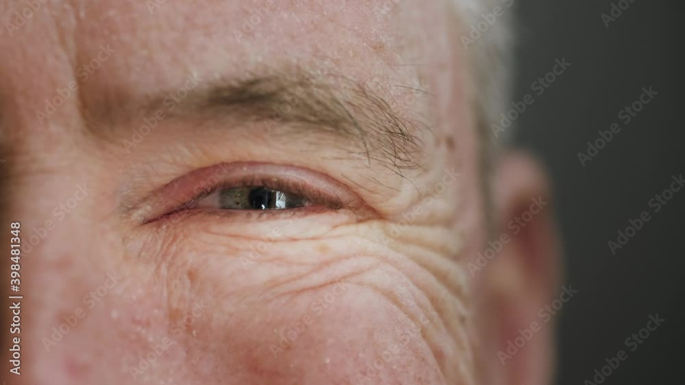 Extreme close up of happy and satisfied old man smiling with blue eye. Elderly mature male senior citizen with wrinkles laughing. Concept of health care, covid-19, retirement. Slow motion, macro, 4K.