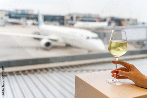 Female hand holding a glass of wine near window with a view to an aircraft