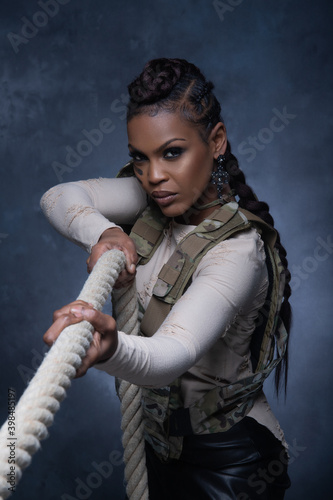 Sexy girl wearing military style vest posing with rope and looking into the camera in studio