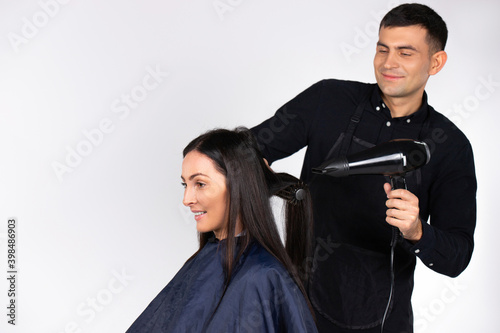 A professional male hairdresser dries a young woman's hair with a foen. Gender stereotypes. White background. photo