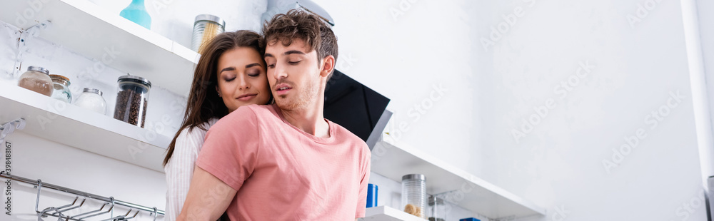 Brunette woman with closed eyes standing near boyfriend in kitchen, banner