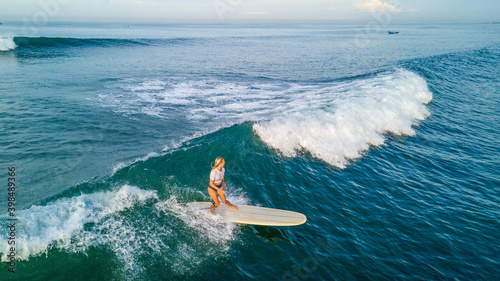 Drone shot of blonde surfer girl surfing on longboard at sunrise on Canggu beach, Bali