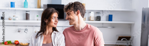 Smiling man looking at girlfriend in kitchen, banner