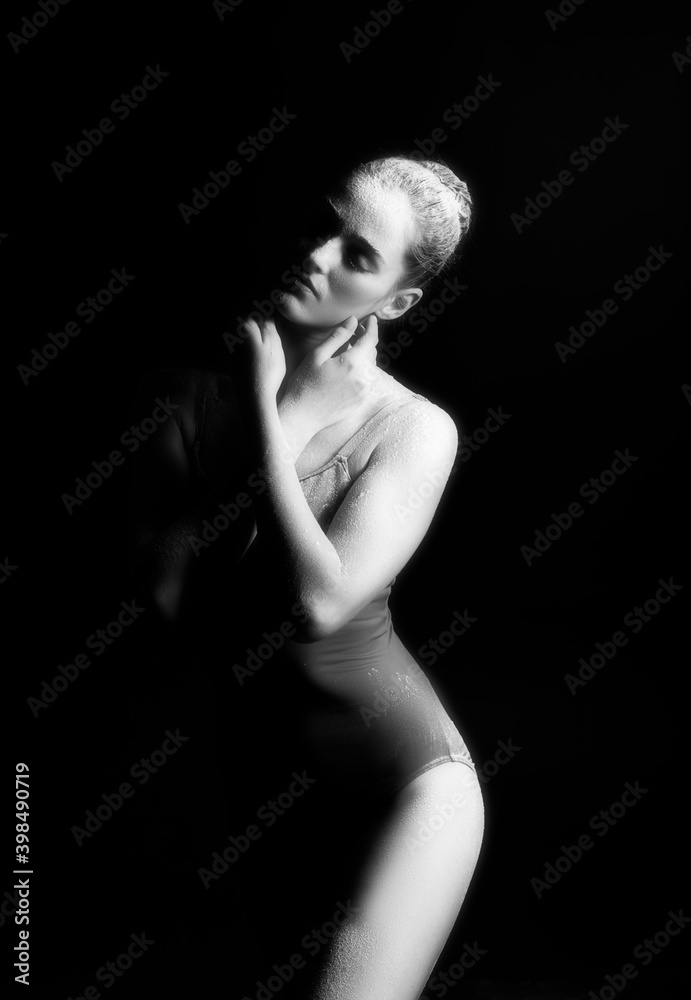 Naklejka premium A high contrast photo of a ballet dancer girl wearing a bodysuit with her body covered in flour against a black background. Artistic, commercial, monochrome design