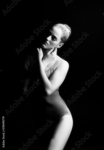 A high contrast photo of a ballet dancer girl wearing a bodysuit with her body covered in flour against a black background. Artistic, commercial, monochrome design