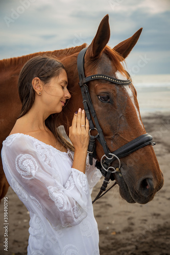 Portrait of beautiful woman and brown horse. Caucasian woman hugging and stroking horse. Beach in Bali, Indonesia