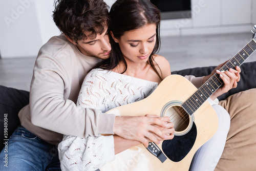 Young couple playing acoustic guitar on sofa together