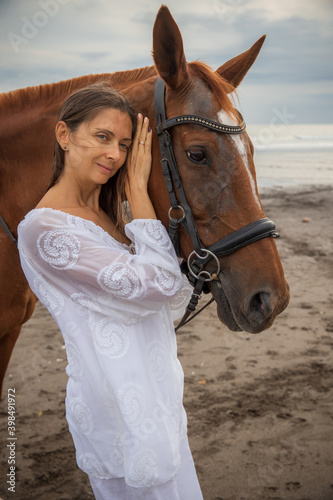 Portrait of beautiful woman and brown horse. Caucasian woman hugging and stroking horse. Love to animals. Beach in Bali, Indonesia