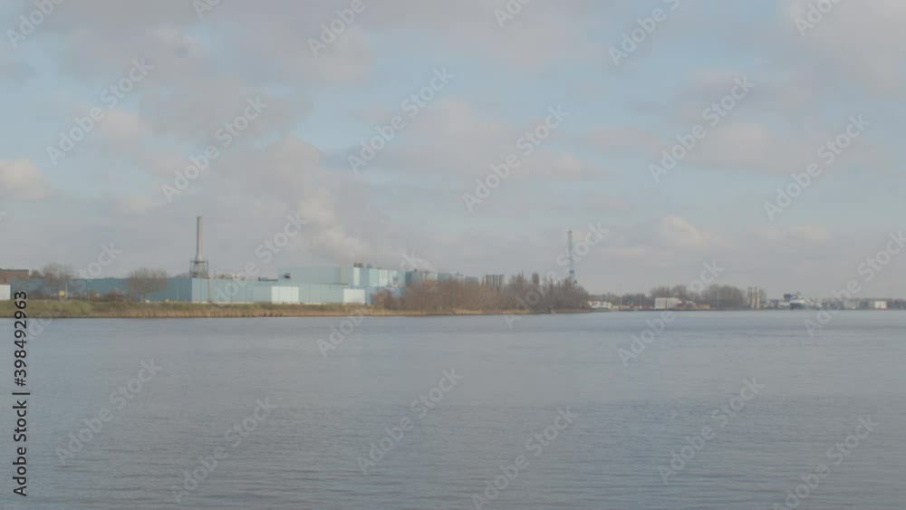 White smoke rising from industrial building on river shore - wide White smoke rising from industrial building on river shore - wide