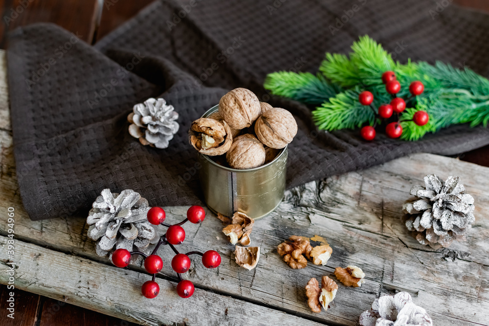 Walnuts in a tin, whole and split, next to the filling and shell. Presented in a New Year's composition with cones, red berries and a sprig of a Christmas tree. Home storage of winter preparations Walnuts in a tin, whole and split, next to the filling and shell. Presented in a New Year's composition with cones, red berries and a sprig of a Christmas tree. Home storage of winter preparations