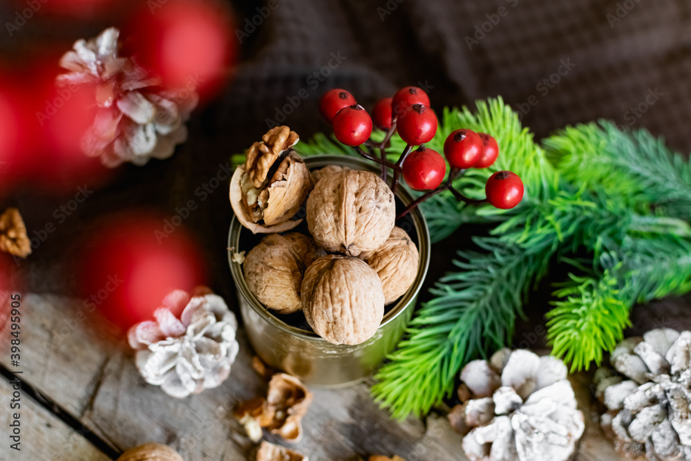 Walnuts in a tin, whole and split, next to the filling and shell. Presented in a New Year's composition with cones, red berries and a sprig of a Christmas tree. Home storage of winter preparations