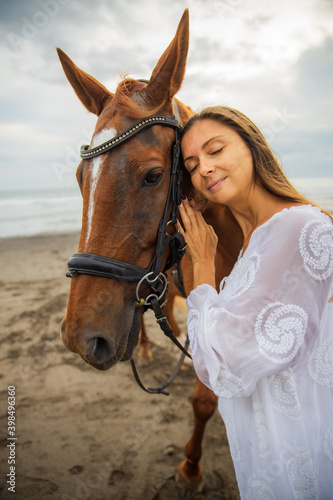 Portrait of beautiful woman and brown horse. Caucasian woman hugging and stroking horse. Love to animals. Beach in Bali, Indonesia