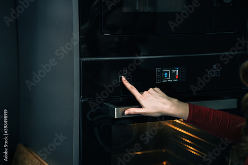 Cropped view of woman hand regulate temperature and timer on built in oven equipment, standing near kitchen appliance in modern interior house, cooking food