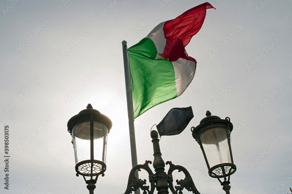A pole with the Italian flag on which also hangs a face mask to honor all the victims of the pandemic.