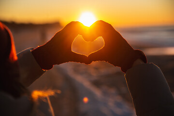 Woman hands in red winter gloves Heart symbol shaped Lifestyle, Winter Solstice and Feelings concept with sunset light nature on background