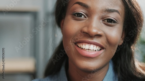 Close up portrait of young african american woman looking at camera with snow white smile sitting on office background.