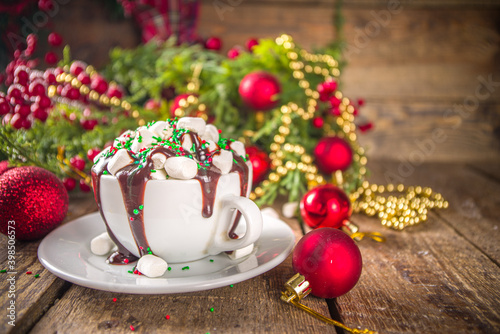 Christmas hot chocolate. Crazy shake styled hot chocolate cup with a lot of marshmallow, chocolate drizzles and green red sugar sprinkles, Christmas New Year decorate background festive bokeh effect