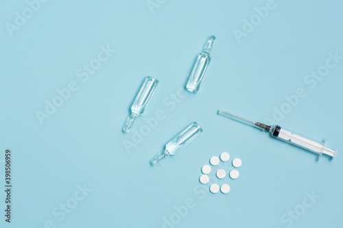 White pills, ampoules and syringe on a light blue pastel background. Medical banner. Concept of medicine and healthcare. Copy space.