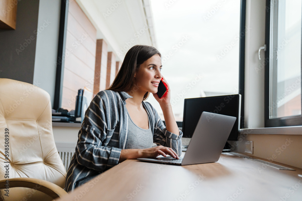 Charming happy woman talking on cellphone while working with laptop Charming happy woman talking on cellphone while working with laptop