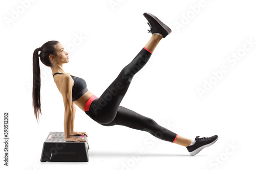 Fototapeta Naklejka Na Ścianę i Meble -  Young woman exercising on a step aerobic platform and lifting one leg up