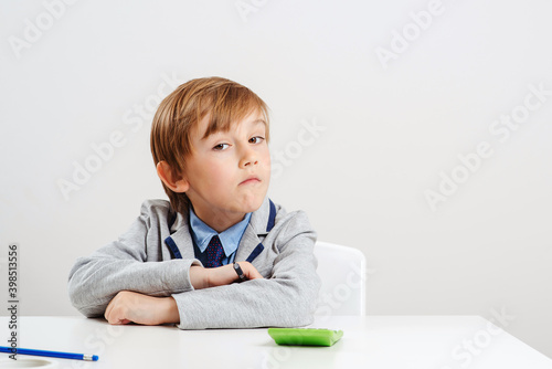 Boy in suit sitting at the desk. Young business boy dream about future profession. Education concept.
