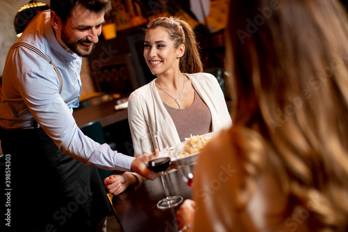 Young waiter serving food to female customers in the restaurant