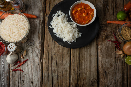 Fototapeta Naklejka Na Ścianę i Meble -  View from above of black round plate with boiled rice and hot tasty chicken curry on rustic wooden table with lime and spices background. Classic Indian recipe. Space for text.