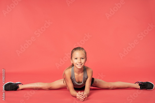 Cute sporty girl doing splits against red background photo
