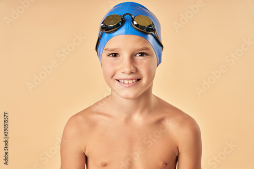 Cheerful boy swimmer standing against light orange background
