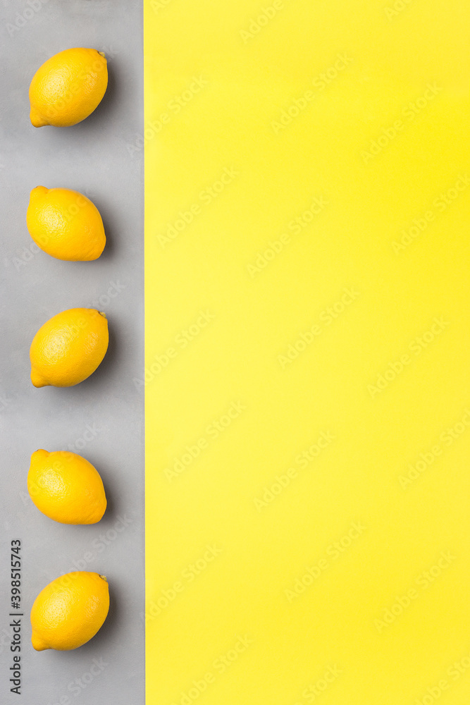 Yellow paper and gray concrete texture, fresh lemons on gray background, colors of year 2021, vertical, copy space