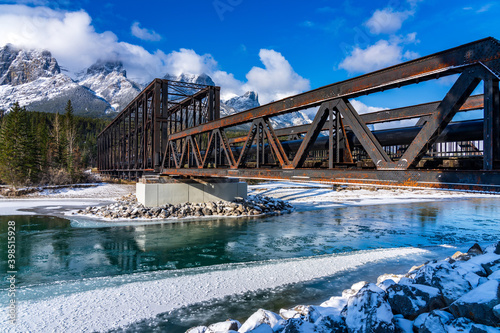 Drift ice floating on Bow River in early winter season sunny day morning. Clear blue sky, snow capped Mount Rundle mountain range in background. Landscape in Canmore Engine Bridge, Alberta, Canada.