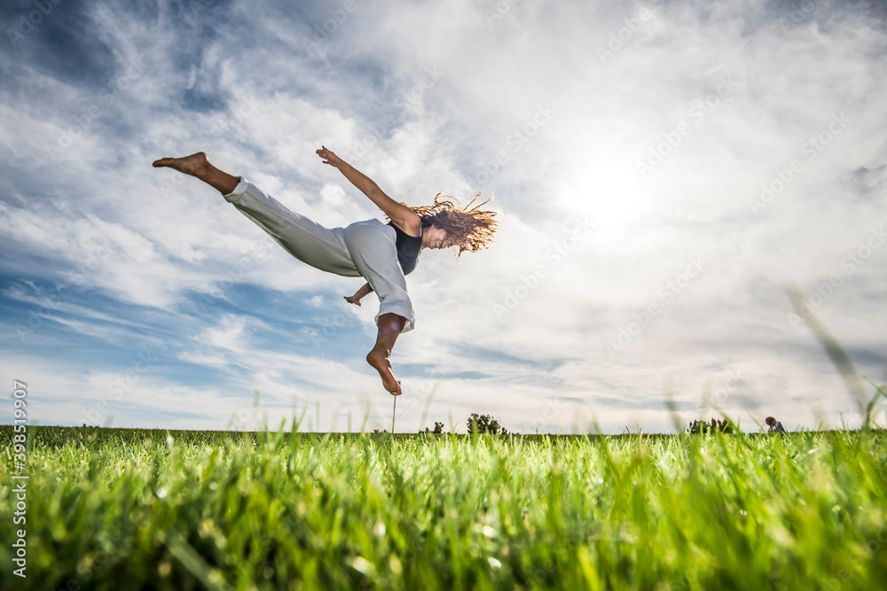 Female athlete jumping in mid-air over grass at park against cloudy sky Female athlete jumping in mid-air over grass at park against cloudy sky