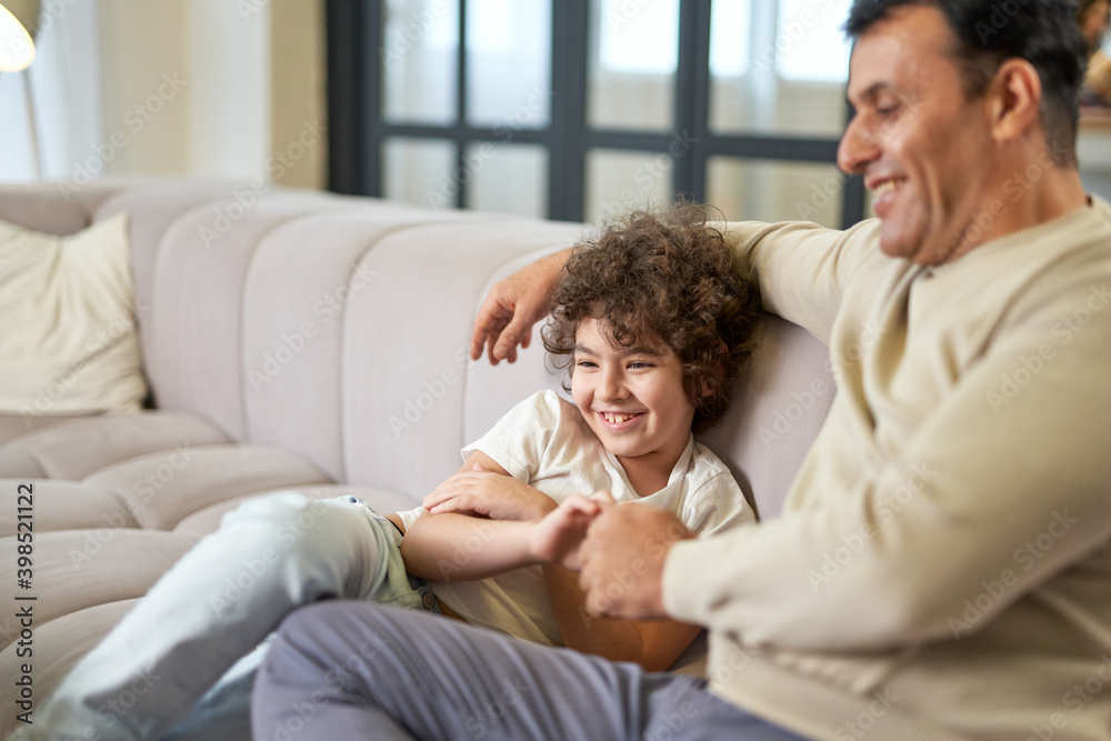 Giggling moments. Happy latin middle aged father spending time with his son, playing with the child in the living room at home Giggling moments. Happy latin middle aged father spending time with his son, playing with the child in the living room at home