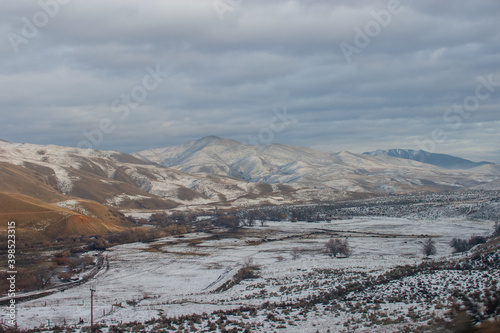 The beautiful mountain valley is covered with snow at sunset  there are small houses  cattle walks.