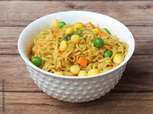 Mixed Veg Maggie Noodles, Instant Noodles cooked with veggies and then served in a bowl over a rustic wooden background, selective focus photo