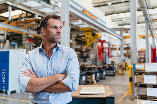 Confident male entrepreneur with arms crossed looking away while standing in factory