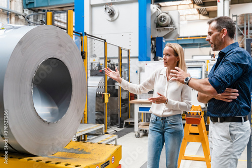 Female entrepreneur and male colleague examining steel roll while standing in factory photo
