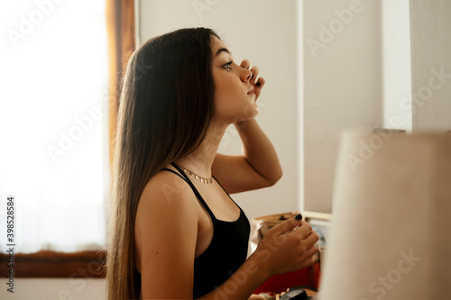 Long hair teenage girl applying make up while standing at home