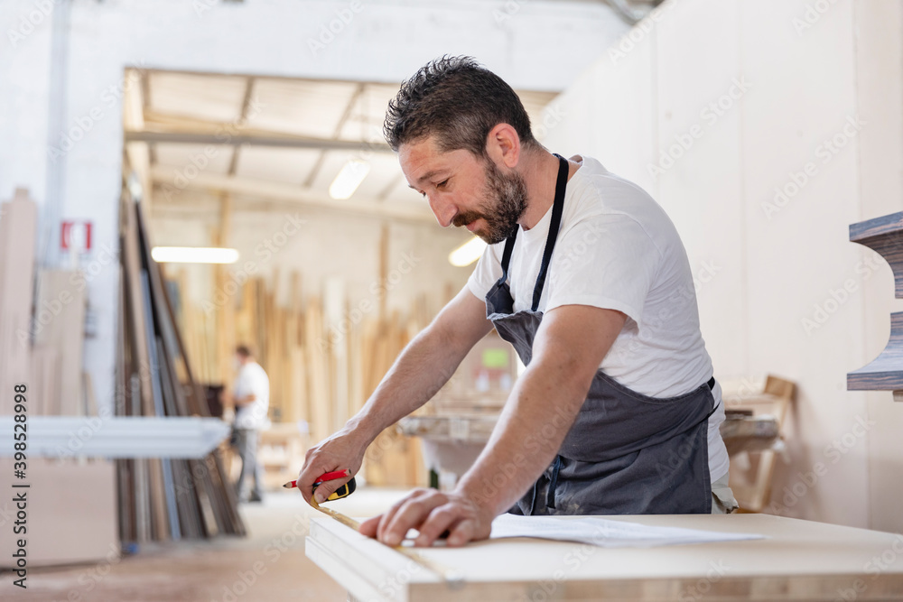 Man measuring wood with measurement tape while standing at workshop Man measuring wood with measurement tape while standing at workshop