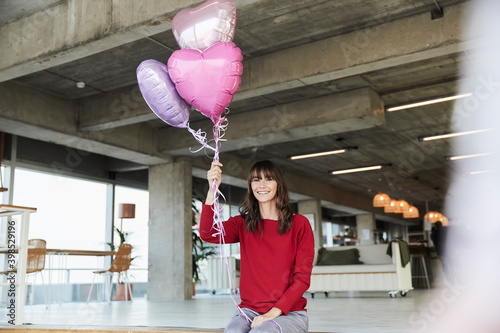 Mature woman holding heart shape helium balloon while sitting at home photo